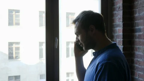 41 Young man talking on the mobile phone walks along bright window Stock-Footage 103435271