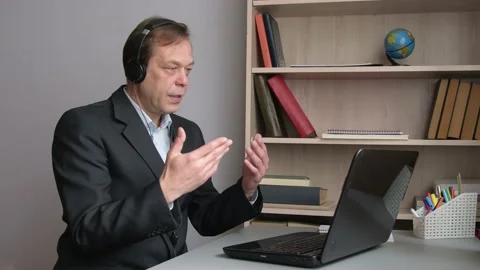 A 45-50-year-old man communicates via video at a laptop with headphones, gesture Video stock 219332912
