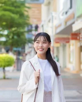 4:5 vertical image of smiling young Asian businesswoman in white blazer wal.. Stock Photos
