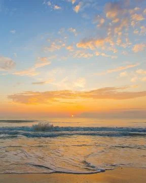 4:5 vertical image of sunset beach with soft sea waves and vibrant blue-ora.. Stock Photos