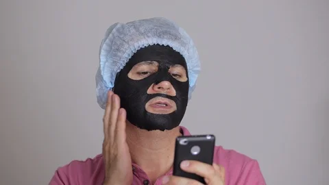 A 45-year-old man, applying a rejuvenating cosmetic mask of black tissue to his Stock Footage 93378855