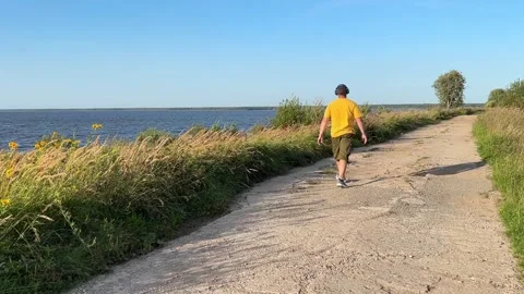 45-year-old man wearing headphones walks slowly along the seashore, summer time. Stock Footage 283947063