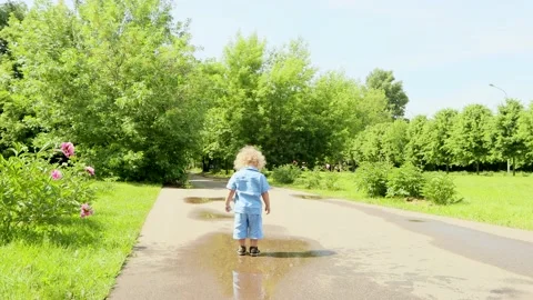 4K. A 2 year old blond boy with curly hair runs through puddles summer day Stock Footage 133903471