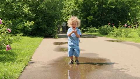 4K. A 2 year old blond boy with curly hair runs through puddles on summer day Stock Footage 133904567