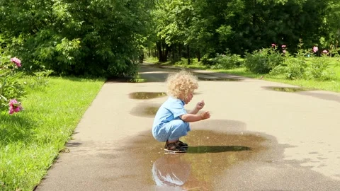4K. A 2 year old blond boy with curly hair runs through puddles on summer day Stock Footage 133906602