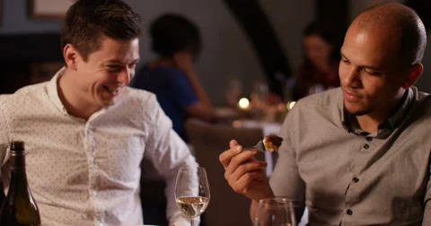 4K 2 Young men laughing &amp; enjoying a meal out, man offers his companion a taster Stock Footage 62889965