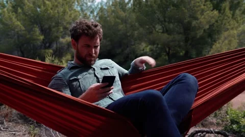 4K 24fps video. Camera moving next to a young man lying in a hammock using th Stockbeeldmateriaal 132516575