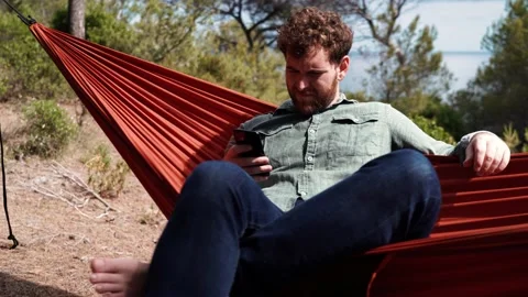 4K 24fps video. Camera moving next to a young man lying in a hammock using th Stockbeeldmateriaal 132516613