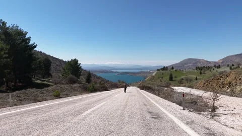 4K 60fps Low Altitude Drone Flyover Over Man Sitting on Asphalt Road Toward Lake Видео 345235850