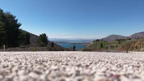 4K 60fps Low Angle Static Slow Motion Shot of Man Walking on Road Toward Lake Stock Footage 345241671