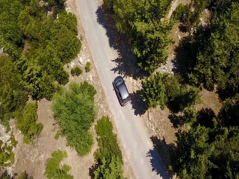4K aerial drone footage small car corners rural road in dense forest Stock Footage