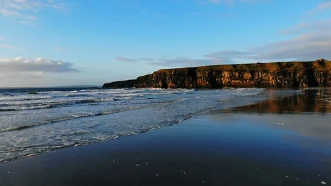4k aerial flying low over beach and waves towards cliffs at sunset Video stock 89235458