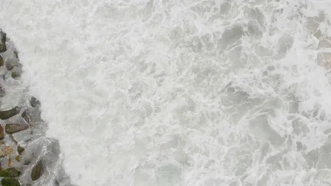 4k Aerial Top Down Pull up shot of  waves crashing in the stone beaches of Stock Footage 125377800
