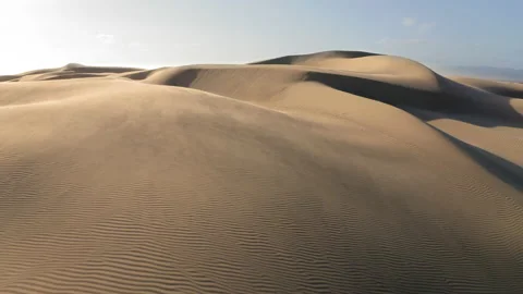 4K aerial on the wind blowing the sand off the top of wavy golden sand dunes Stock Footage 134572083