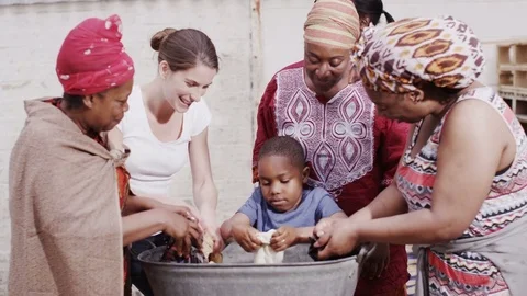 4K African family with charity worker work together to wash clothes by hand Stock Footage