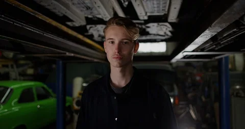 4K Apprentice mechanic standing under vehicle ramp with serious expression Stock Footage 112970555
