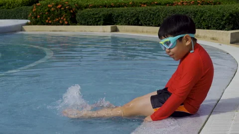 4K, Asian boy in a red black bathing suit is swinging his feet in the water 스톡 동영상 204033418