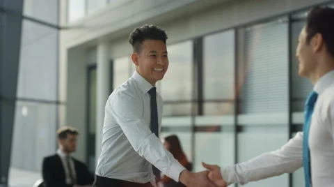 4K Asian businessmen meet & shake hands in crowded area of large modern office Stock Footage