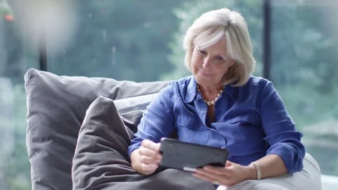 4K Attractive mature woman with computer tablet browsing the internet at home Stock Footage