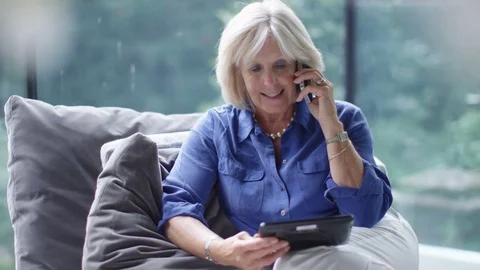 4K Attractive mature woman making a phone call with computer tablet in her hand Stock Footage