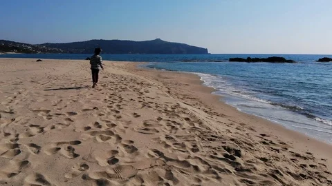 4k barefooted child running Away from drone flying view on sea shore sandy beach Stock Footage 105775009