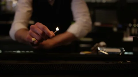 4K Barman Using A Match To Set Light To Row Of Shot Glasses With Clear Liquor Video stock 75629507