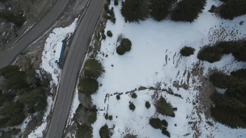 4K Bird’s-Eye Drone Shot Descending and Rotating Over Snowy Mountain Road 動画素材 326540868
