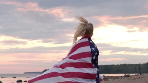 4k. Blonde girl running waving national USA flag outdoors over sunset sky at Stock Footage