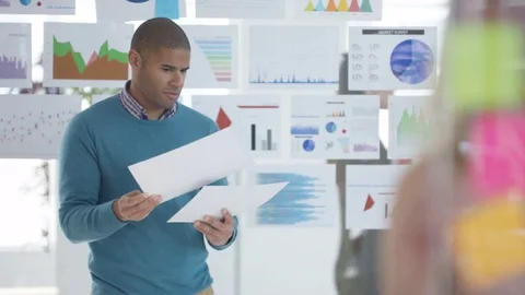 4K Businessman looking at papers in front of screen with charts &amp; graphs Stock Footage 76033739