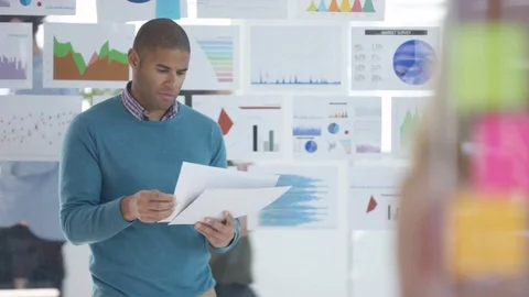 4K Businessman looking at papers in front of screen with charts &amp; graphs Stock Footage 76033745