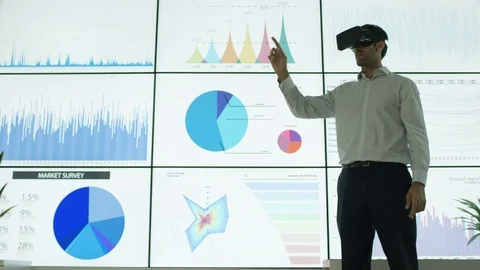 4K Businessman with virtual reality headset in front of video wall with graphs Stock Footage 75972652