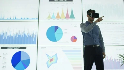 4K Businessman with virtual reality headset in front of video wall with graphs Stock Footage 75972998