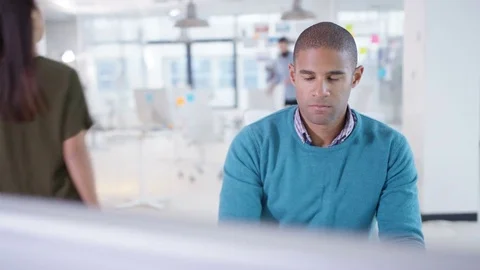 4K Businessman working on computer at his desk with colleagues in a meeting Stock Footage 76046904