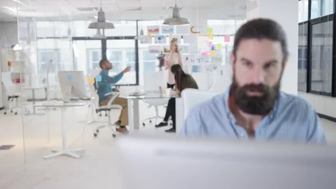 4K Businessman working on computer at his desk with colleagues in a meeting Video stock 76057671