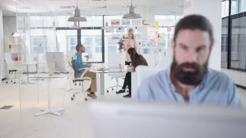 4K Businessman working on computer at his desk with colleagues in a meeting Stock Footage 76057739