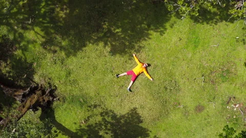 4K camera flying up above man dressed in yellow windbreaker and lying in forest Stock Footage 168779081