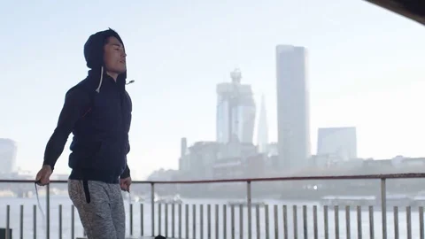 4K Camera tilts down as asian man skips with a jump rope in the city, in slow mo Stock Footage