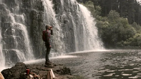 4k of camping man / hiker standing on rock edge viewing waterfall and water pool 動画素材 199620719