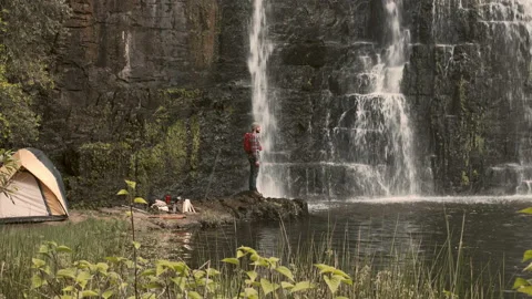 4k of camping man / hiker standing on rock edge viewing waterfall and water pool Stock-Footage 199620731