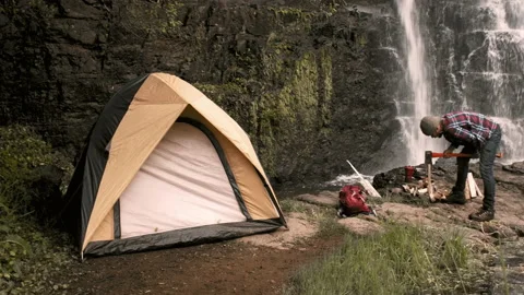 4k of camping man / hiker at waterfall chopping wood for his campfire next ton y 库存影片 199620577