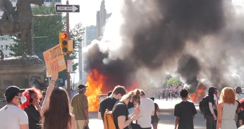 4K CAR ON FIRE WITH PROTESTERS IN MASK REMAINING CALM Video stock 131453591