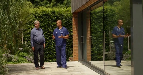4K Caring doctor giving good news to senior man as they walk in hospital garden Stock Footage 81459367