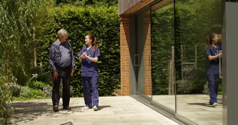 4K Caring nurse giving good news to senior man as they walk in hospital garden Stock Footage 81133370