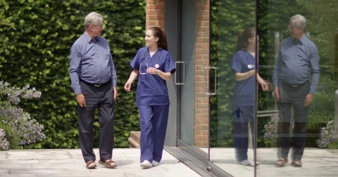 4K Caring nurse giving good news to senior man as they walk in hospital garden Stock Footage 81460083