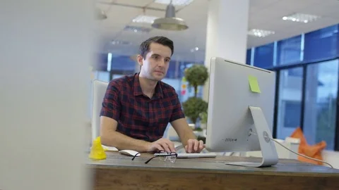 4K Casual businessman working on computer &amp; talking on phone in creative office Stock Footage 75999664