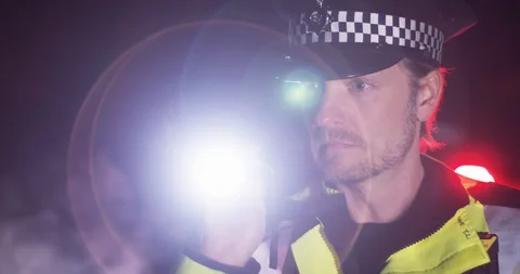 4K Caucasian UK policeman with flashlight investigating a crime scene at night Stock Footage 113680001