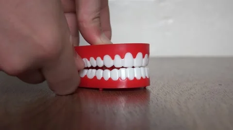 4k chattering red and white teeth being wound up and let go on wooden floor Vídeos de archivo 54660351