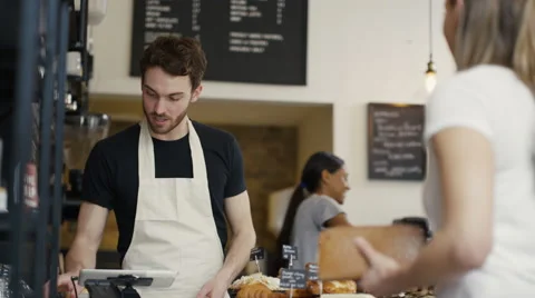 4K Cheerful worker serving customers &amp; taking payment in city coffee shop Stock Footage 61840507