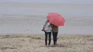 4K Cheerful Young Couple With Red Umbrella Walking On The Beach On A Gloomy Day Stock Footage