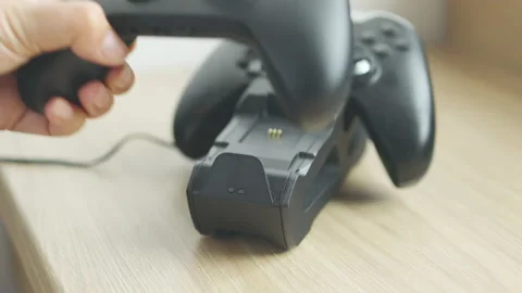 4k. Children hand takes a controller from charging base. Two black controllers Video stock 202208535